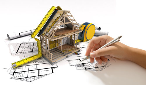 Réglementation RE2020 : maquette de maison en ossature bois posée sur des plans d’architecte, avec mètre ruban et main qui dessine