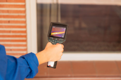 Etude thermique extension : technicien utilisant une caméra thermique devant une fenêtre pour repérer les déperditions de chaleur sur la façade