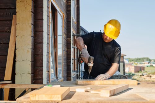 Ouvrier en casque jaune vissant des planches sur un chantier de construction neuve soumis à l'attestation RT bâtiment