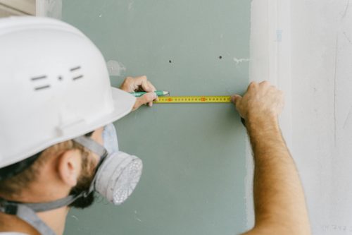 Ouvrier mesurant l'épaisseur d'un panneau isolant sur un mur en plaque de plâtre, illustrant les exigences d'isolation de la RE2020