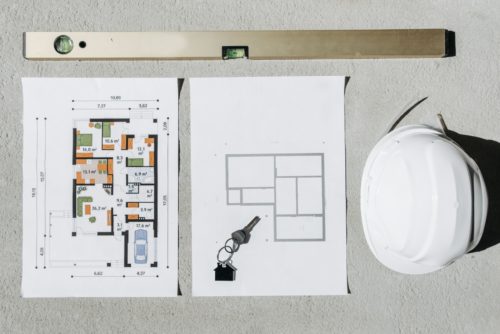 Plans de construction avec surfaces cotées, clés et casque de chantier illustrant le choix entre RT 2012 et RE2020 pour un projet de logement neuf